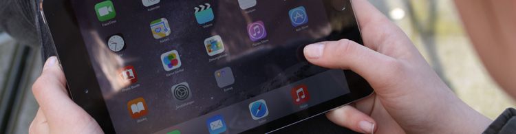 Zwei Hände halten ein iPad, auf dessen Bildschirm verschiedene App-Symbole deutlich zu sehen sind.